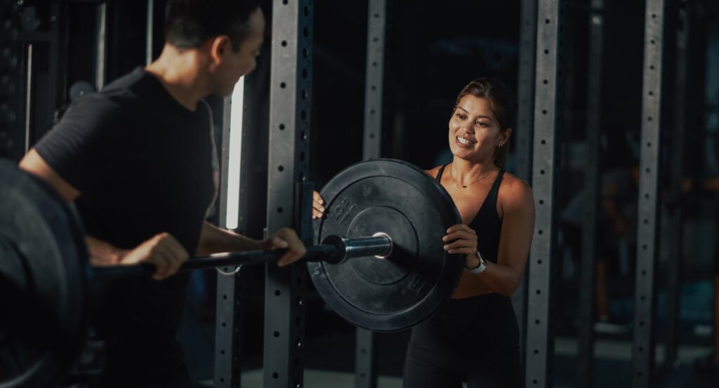 Woman helping man put weights on squatting rack